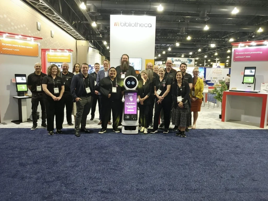 Bibliotheca team poses at the ALA 2025 booth with Romi the robot