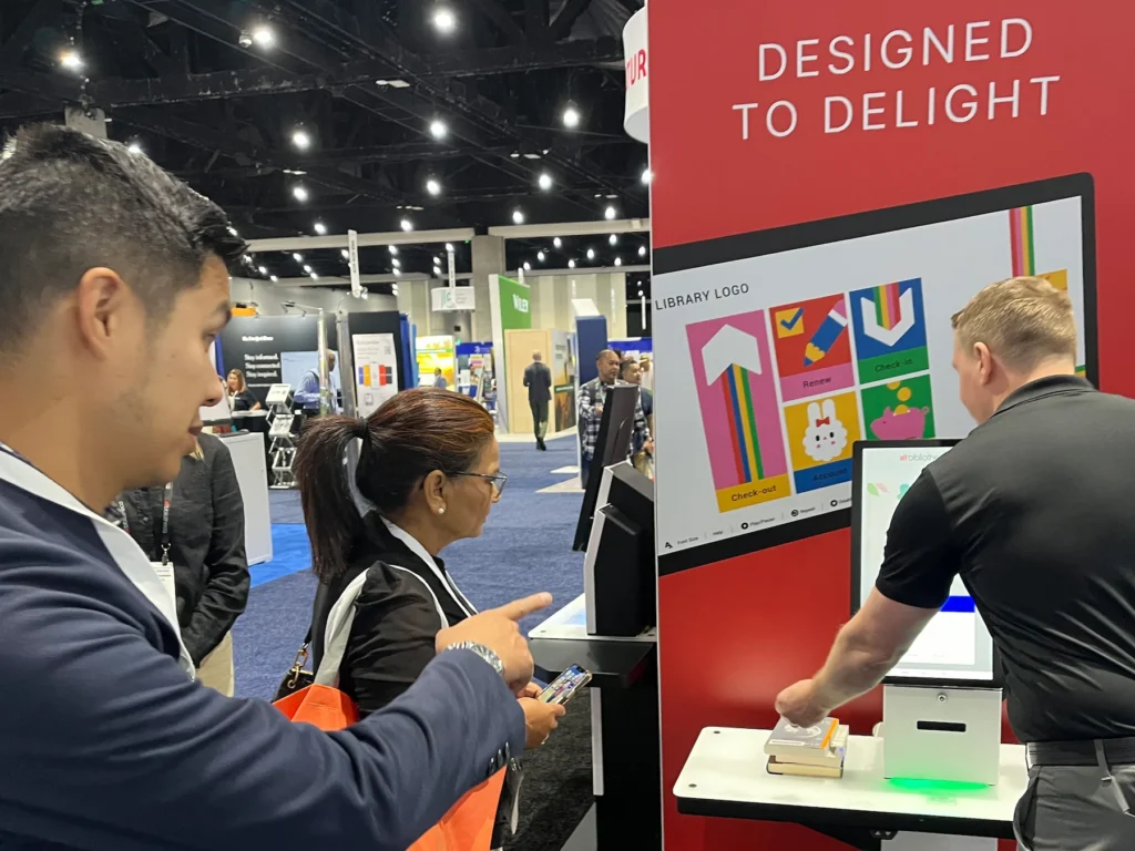 Library professionals exploring the Bibliotheca selfCheck 3000 kiosk at ALA 2024
