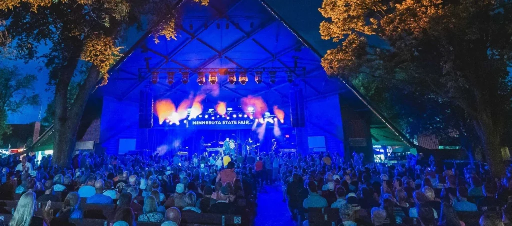 A crowd enjoys a live concert at the Minnesota State Fair under colorful stage lights and evening skies.