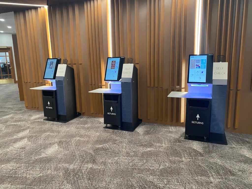 Self-check kiosks with integrated return bins at Redford Township District Library.